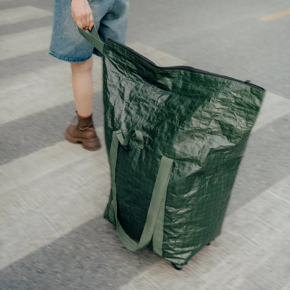 Person holding KOMPISHÄNG, large, green, foldable shopping bag on wheels, made from recycled polypropylene.