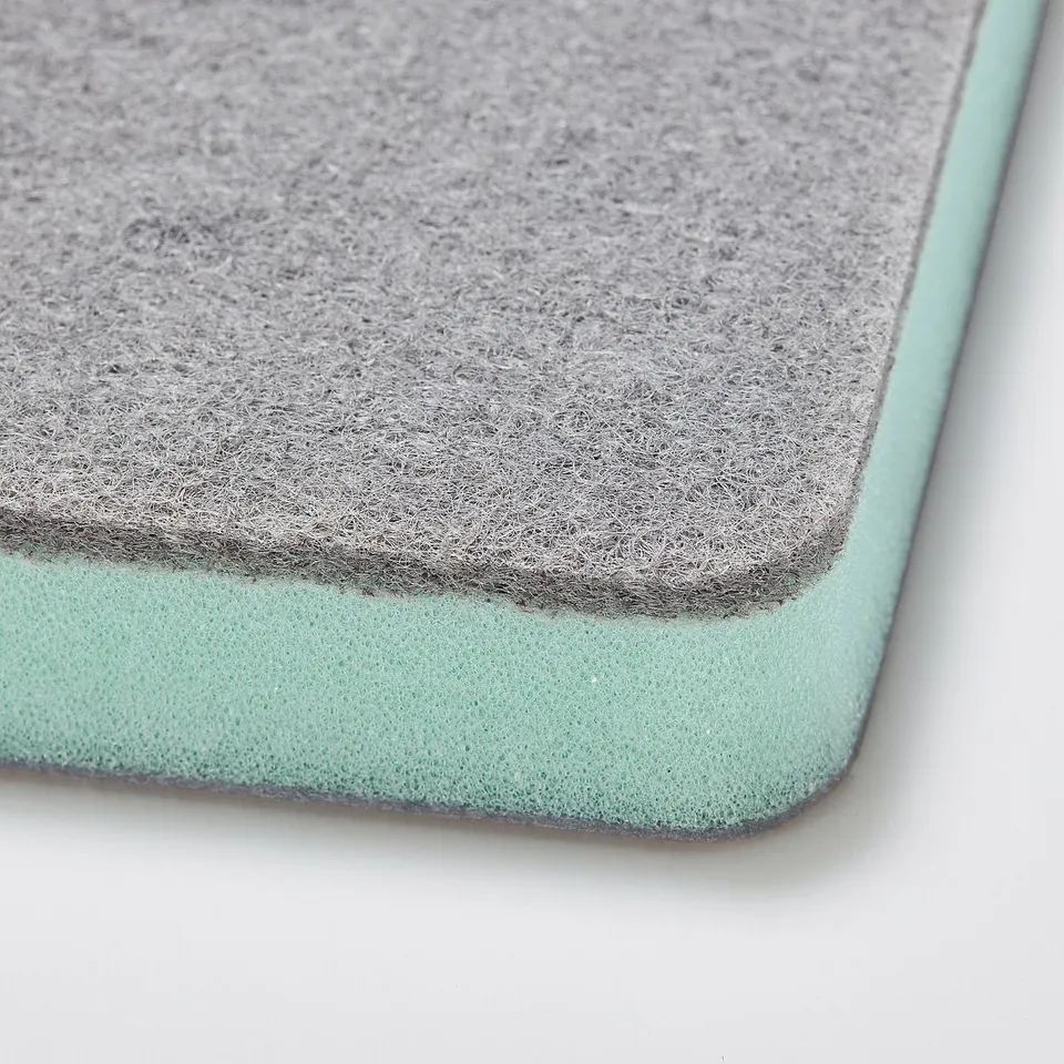 Close-up of a dual-sided cleaning sponge featuring a soft minty green and coarse grey surface, showcasing its textured quality.