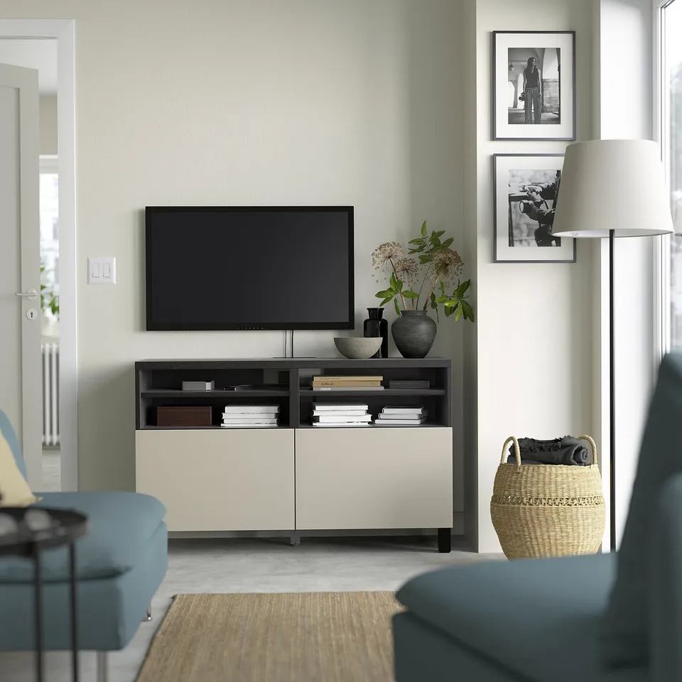 Modern living room with BESTÅ tv bench, flat-screen tv, vases, bowls, blue & beige sofas, and storage.