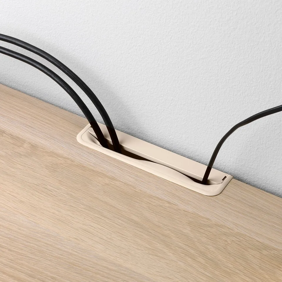 Rectangular cable outlet box mounted on wooden table, holding black cables, managing their route beneath the tabletop.