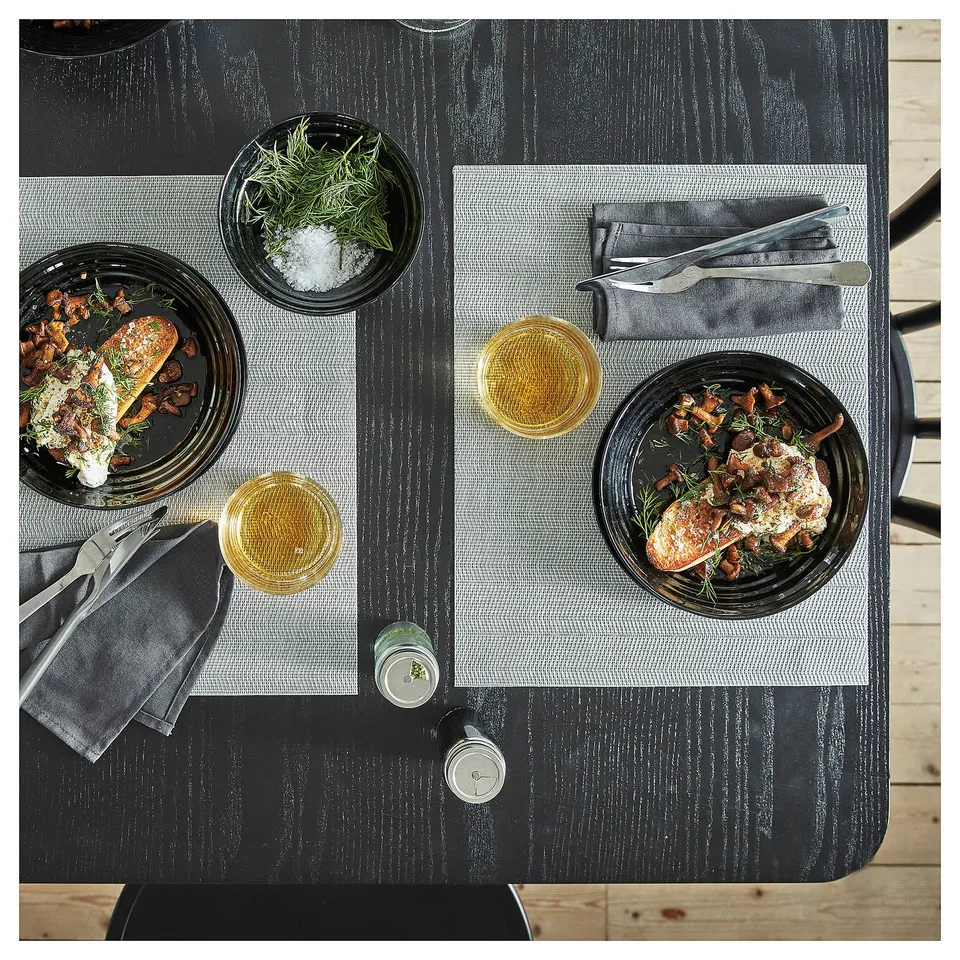 Two plates of food with sauce, mushrooms, and herbs, with glasses of beer, cutlery, and a small dish of herbs and salt on a black wooden table.