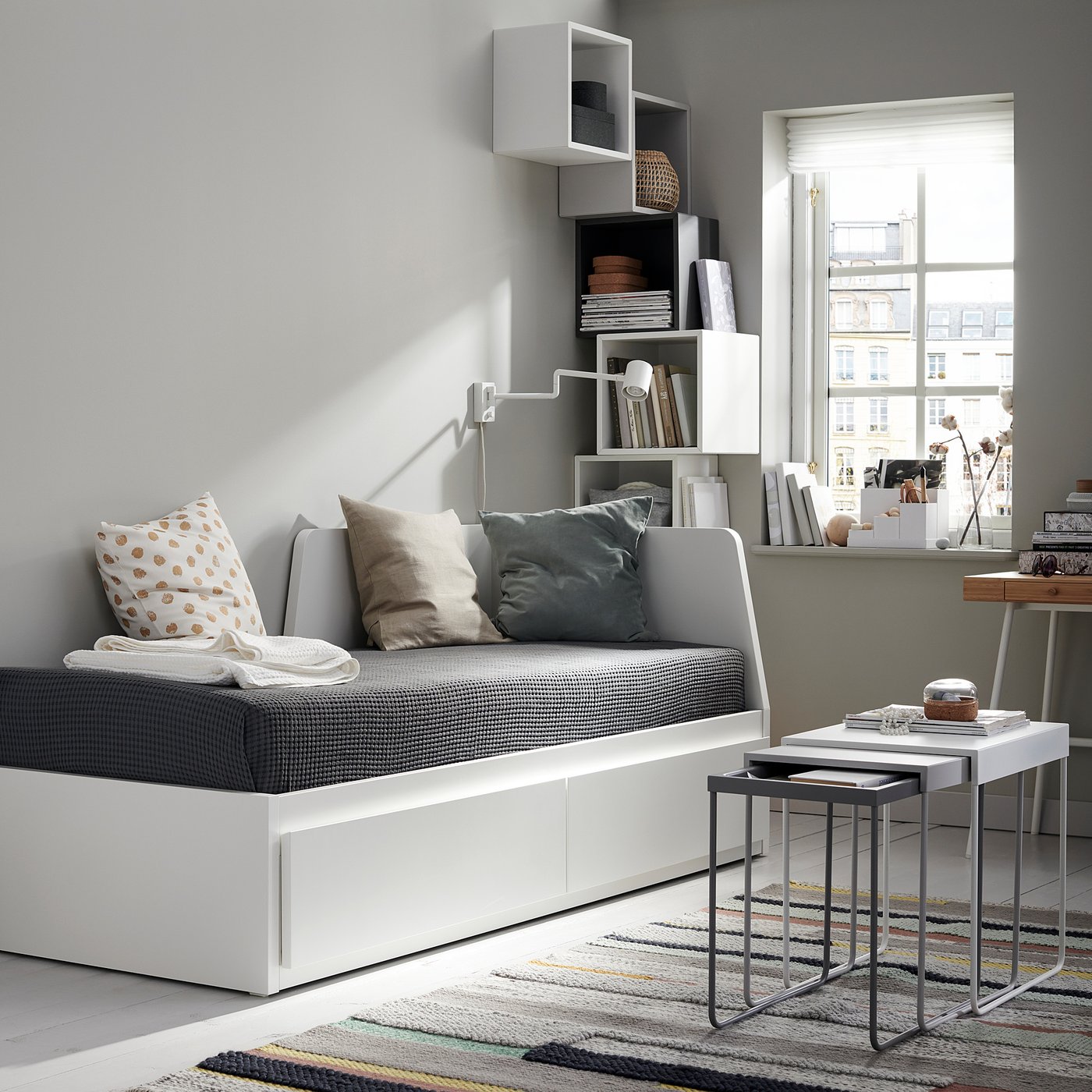 Modern living room with white sofa-bed, grey decor, nesting tables, and city view.