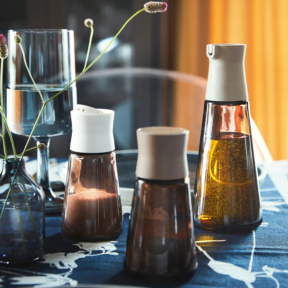 Four brown glass containers with white lids on a tablecloth. Two hold spices, one holds oil, and one is empty, suitable for spices or liquids.