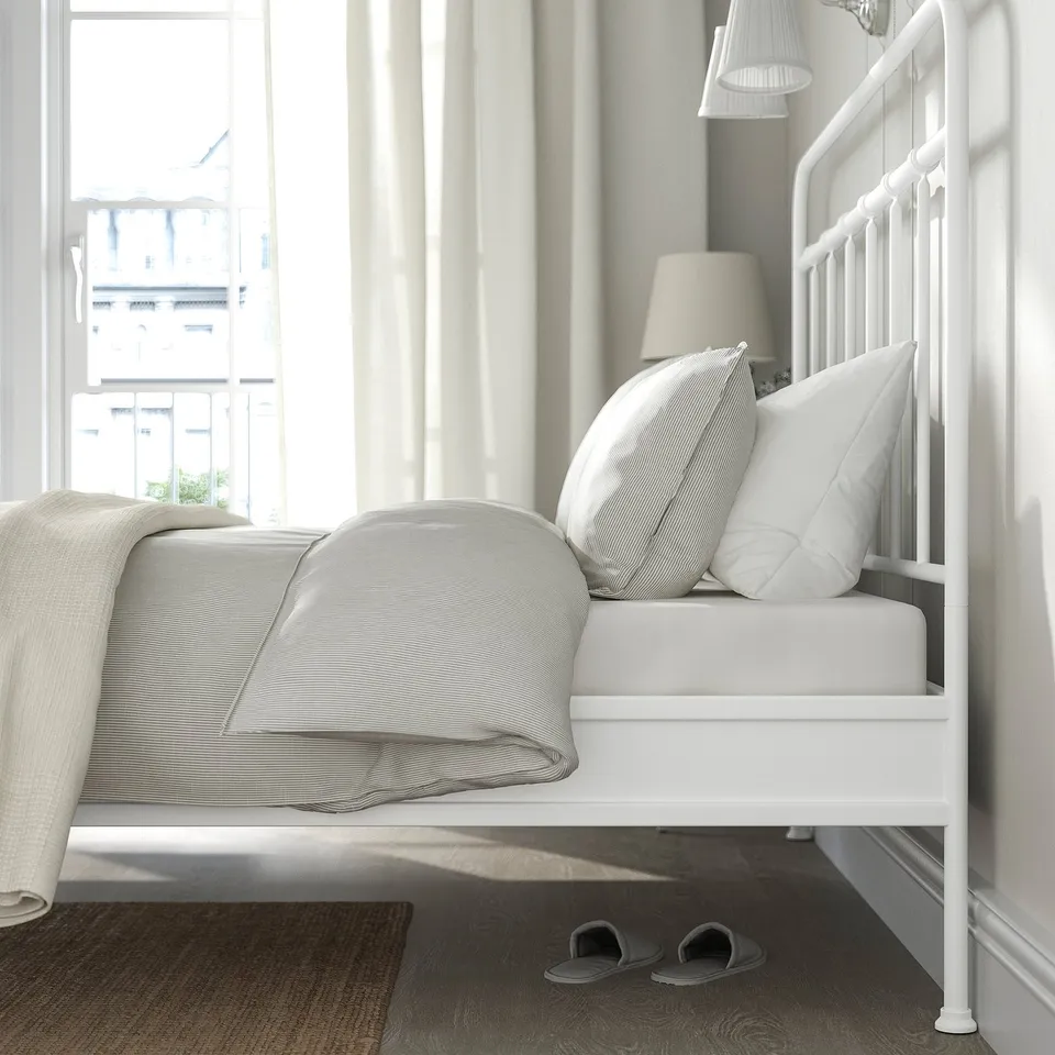 A cosy bed with a white metal frame sits near a window, offering a comfortable spot to relax.
