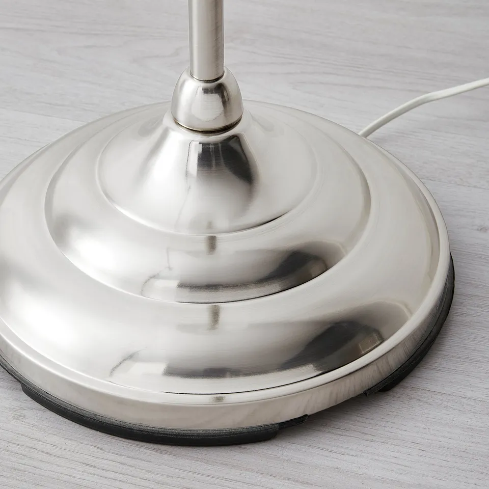 A close-up of a stylish, metallic lamp base on a wooden surface. High-quality finish with smooth texture and shiny nickel plating.