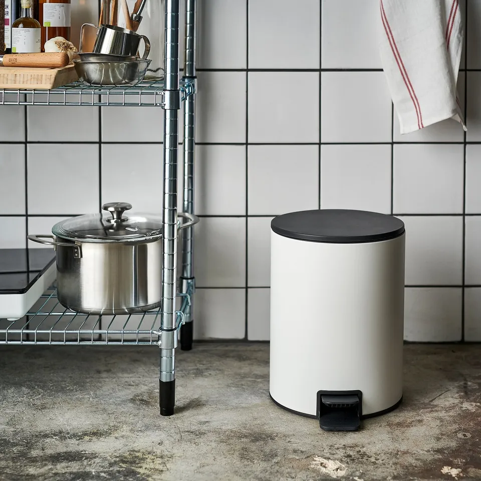 White rubbish can with black lid and foot pedal in kitchen.