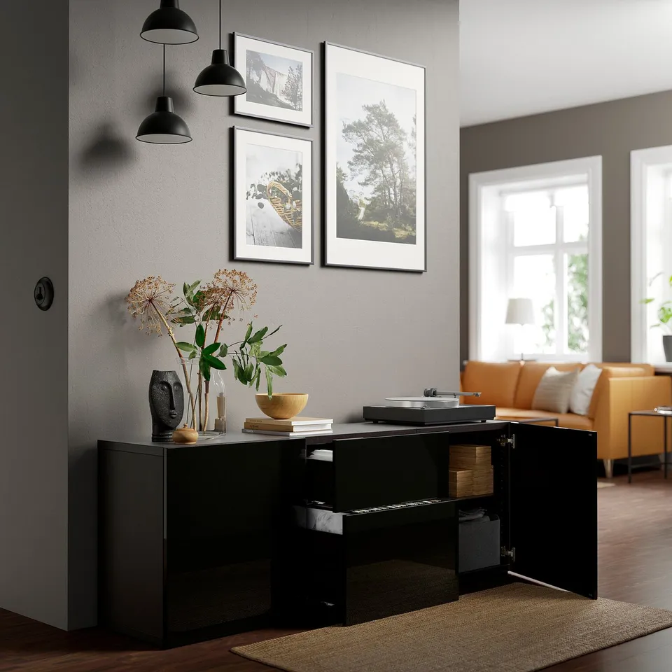 Modern living room with black glossy storage unit. Open shelves, decorative plants, records, and framed art. Bright orange sofa and large windows.