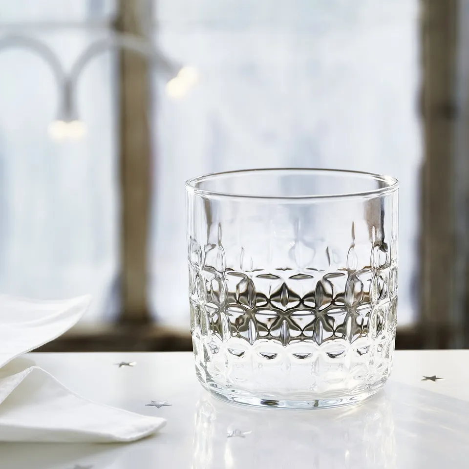 Glass with faceted design sits on reflective surface, surrounded by white napkins.