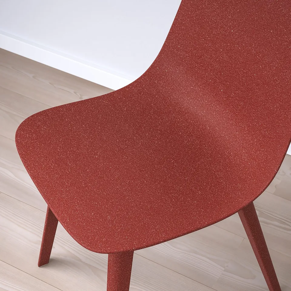 Close-up of a modern red chair with a textured, matte finish on a wooden floor.