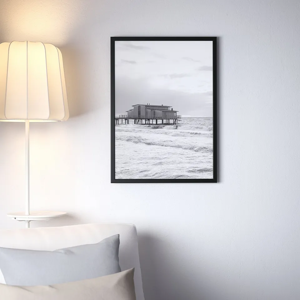 Black & white beach photo on white wall above couch, lamp to left.
