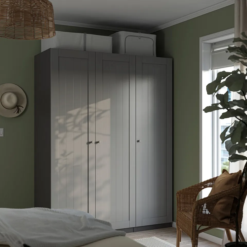 Modern bedroom with tall grey PAX wardrobe, wicker chair, bed, and plant.