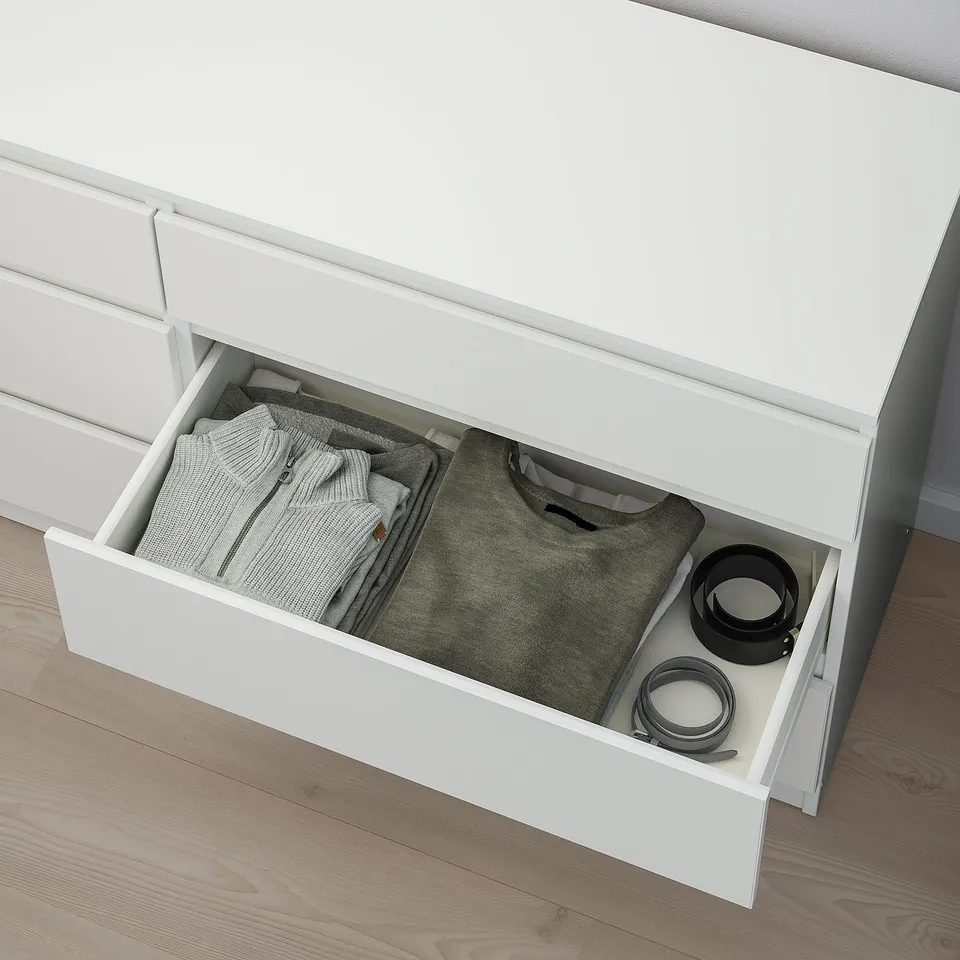 White dresser drawer open, revealing folded clothes and accessories. Safely anchored to wall.