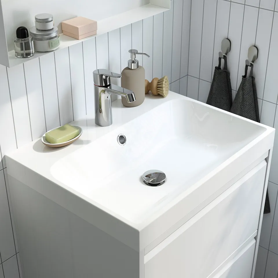 Modern white bathroom sink with sleek tap, soap dish, and soap dispenser on a clean, minimalist countertop.