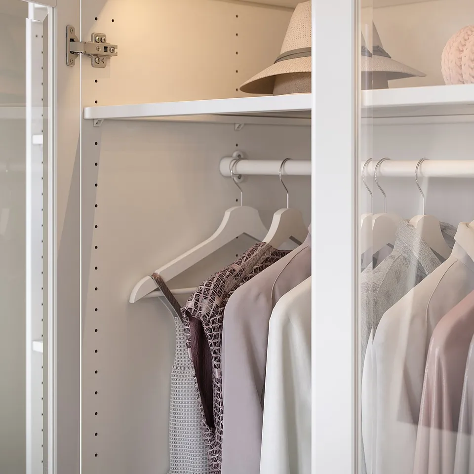 PAX white closet stores clothes, hats in organised shelves and hanging racks.