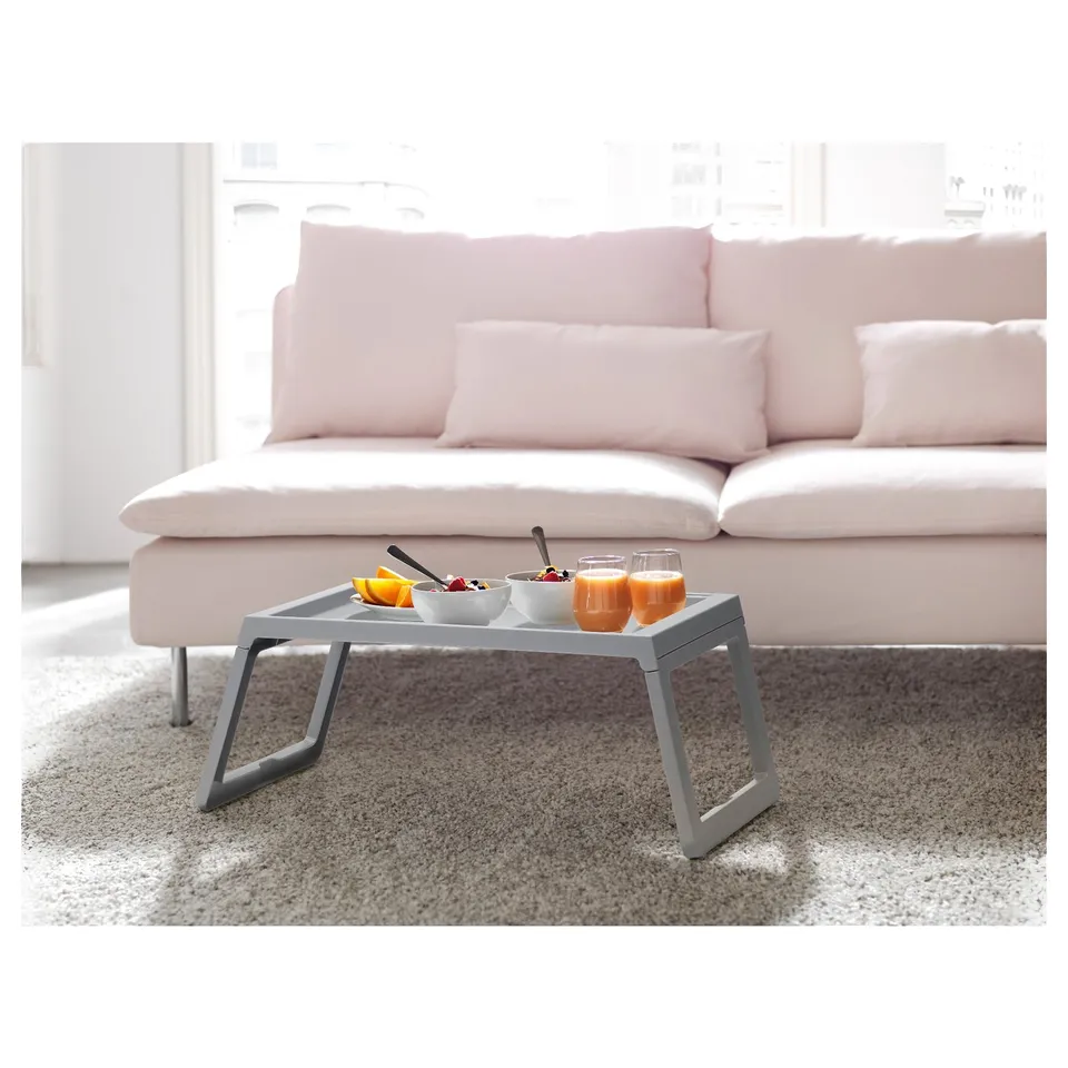 KLIPSK grey bed tray with food, glasses, on pink couch.