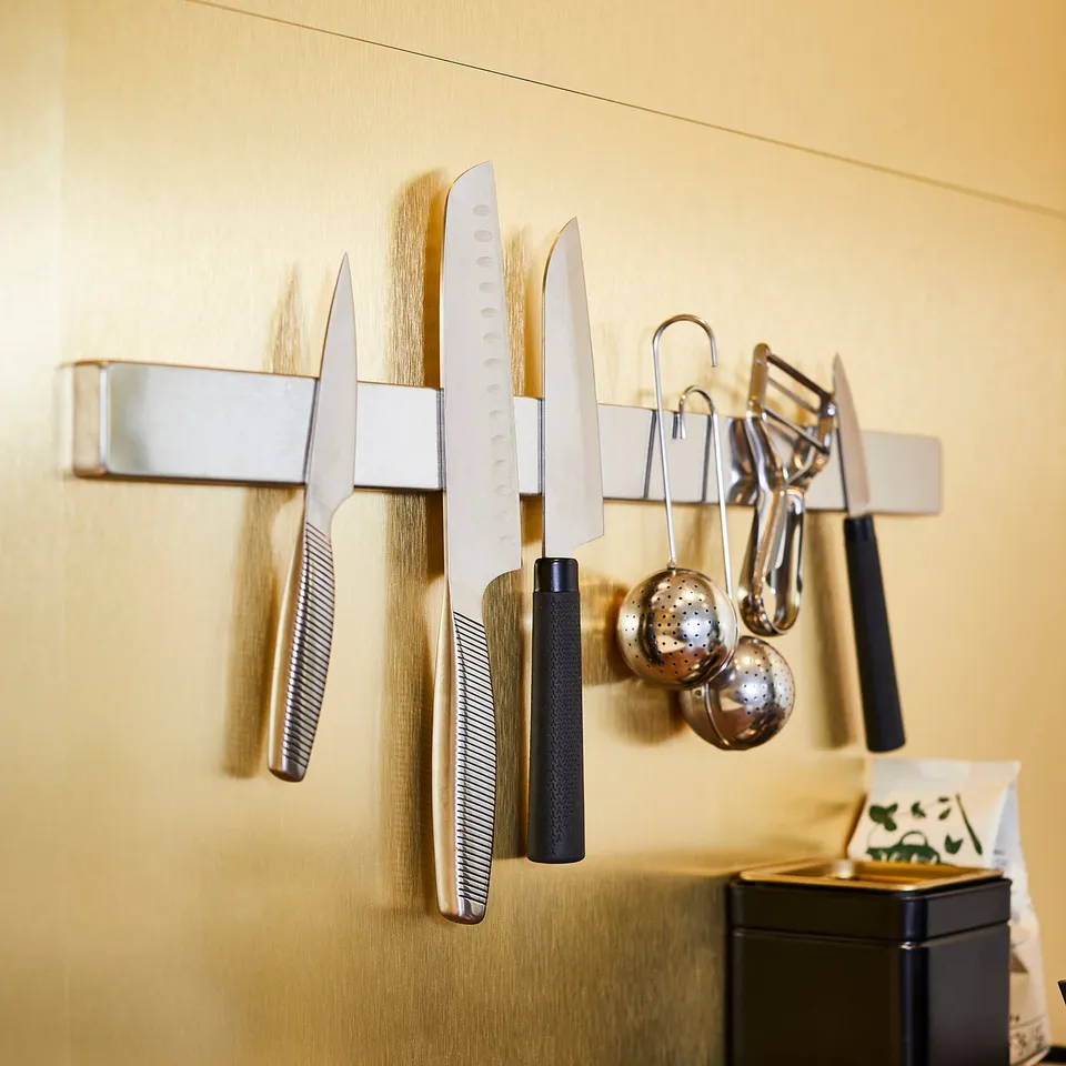Magnetic knife rack on kitchen wall, holding various knives, hooks for utensils. Keeps knives organised and space-efficient.