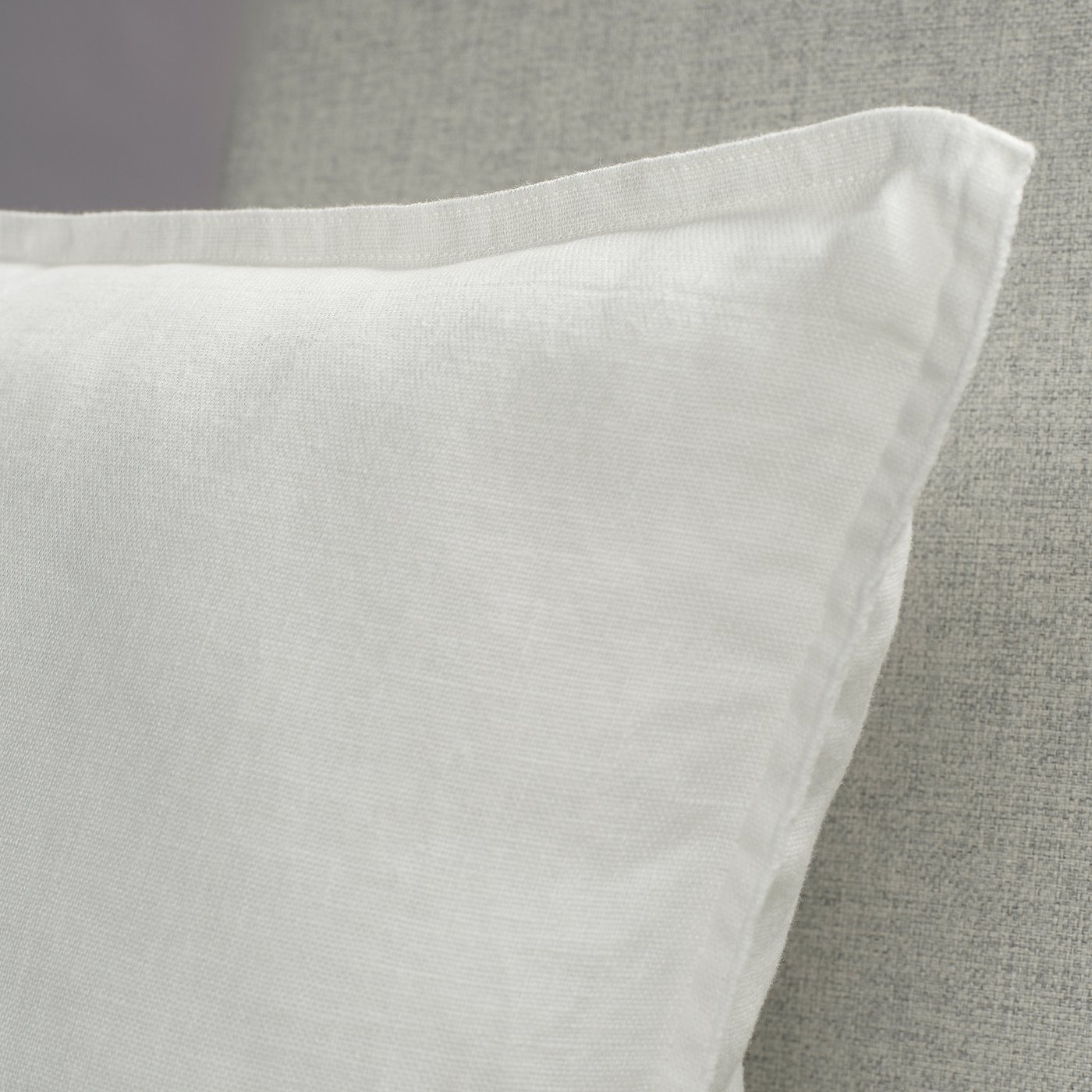 Close-up of a soft, white washed linen pillowcase with neat stitching and a subtle texture, showing high-quality craftsmanship.