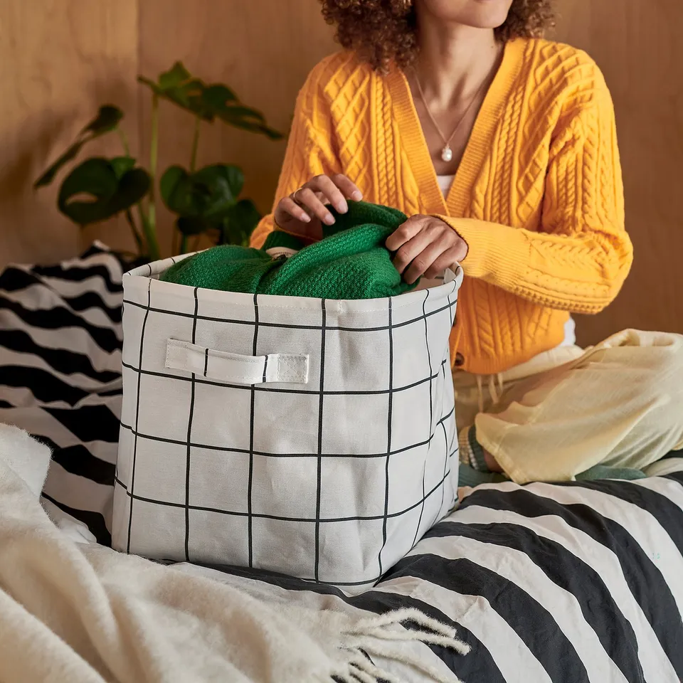 Person organising green towels in white basket on striped bed.
