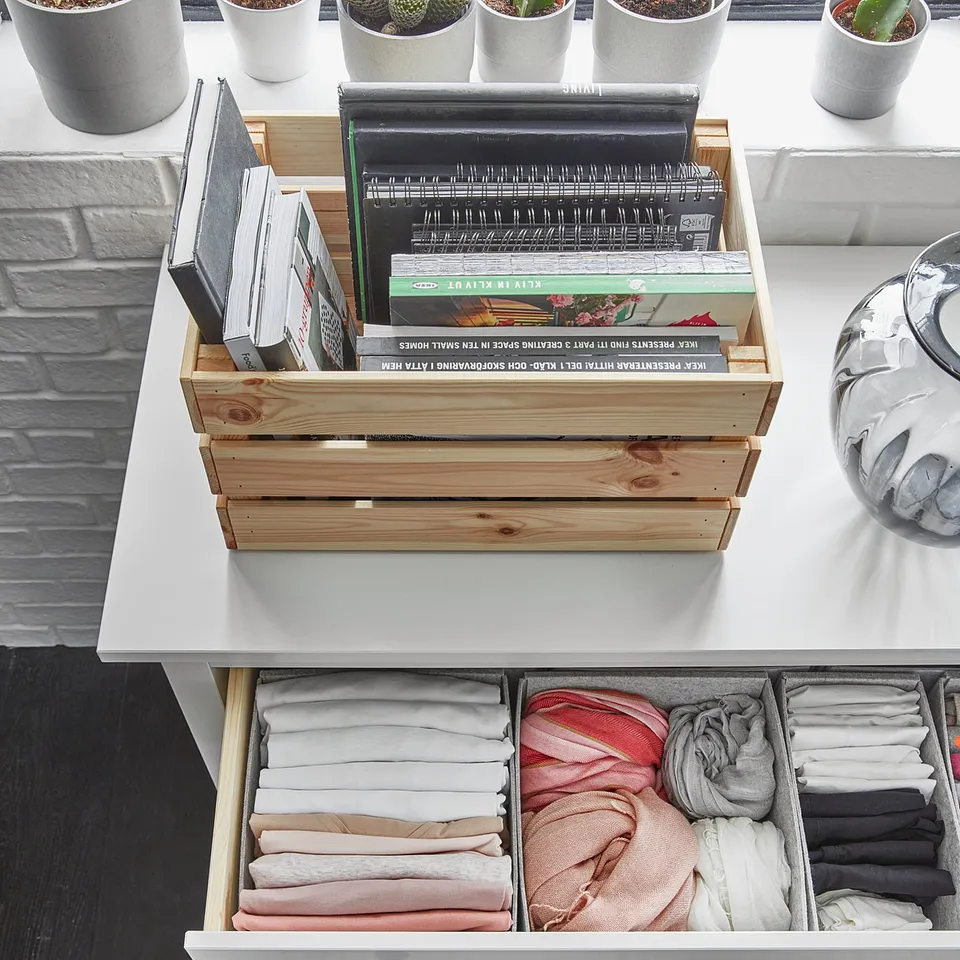 Wooden box with books on a table, open drawer with folded clothes in compartments.