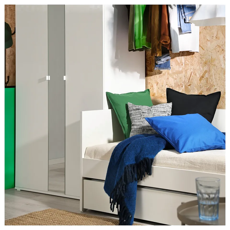 Modern white day-bed with colourful pillows, blue blanket, and wardrobe.