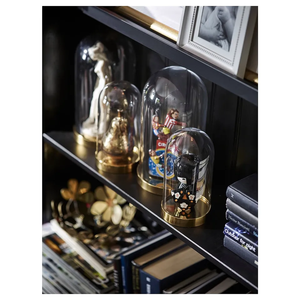 Black bookshelf displaying gold decorative items, glass domes with figurines, and books.