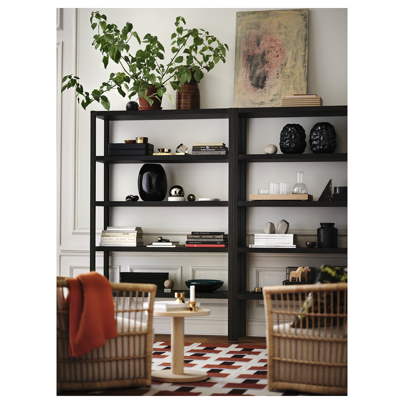 Black shelving unit in 2025, holding books, decor, and plant, between wicker chairs on rug.