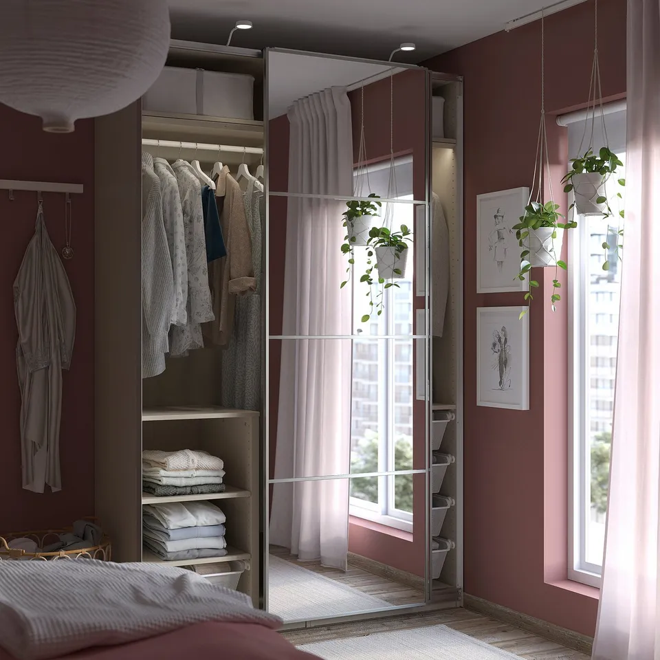 Modern bedroom with red PAX wardrobe, mirrored doors, hanging clothes, shelves with towels, and hanging plants.