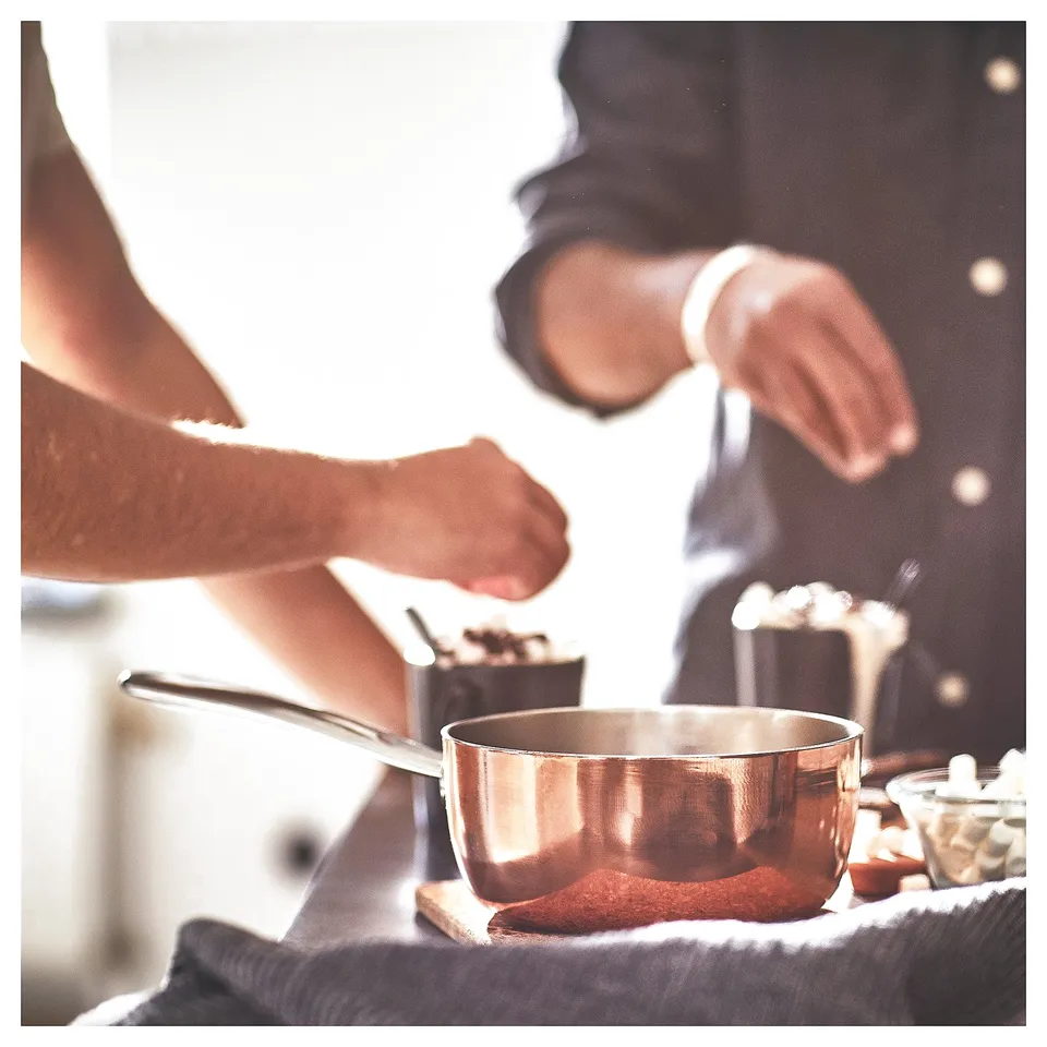 Copper FINMAT saucepan by ilse crawford on stove, hand holding ergonomic handle.