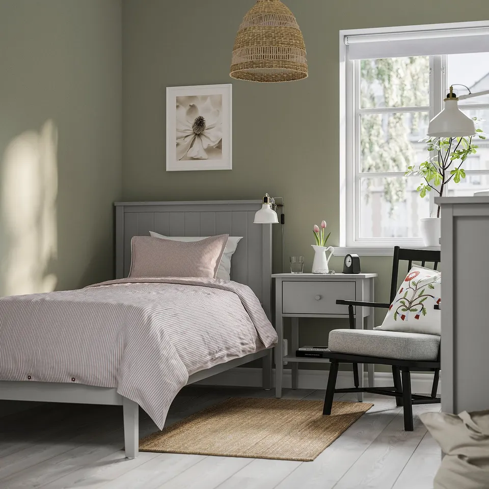 GULLABERG bed in dark grey with grooved headboard, striped linens, green walls, matching furniture, floral pillows, woven lamp, small rug.