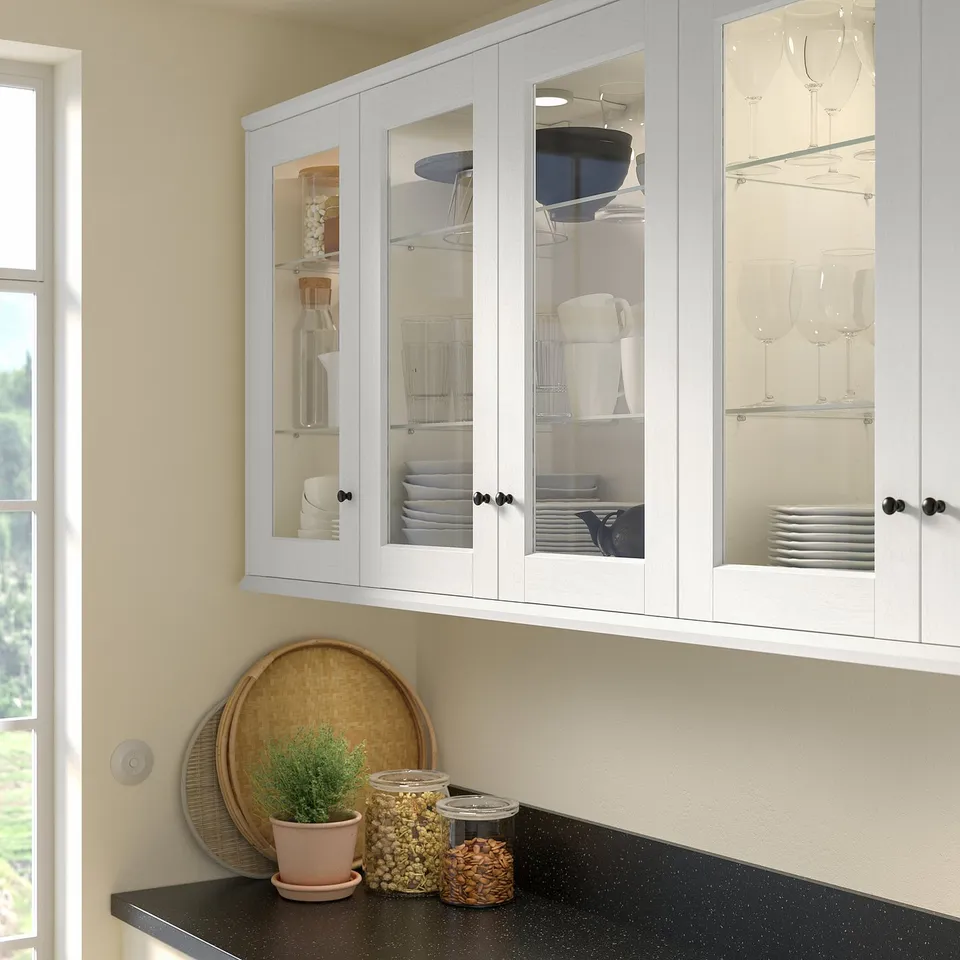White ENKÖPING cabinet with glass doors displaying plates and glasses; includes small potted plant, tray, and jars on countertop.