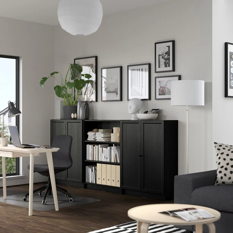 Modern living room with BILLY bookcase, desk, and sofa. Bookcase has open and closed storage, filled with books. Polka-dot pillow adds cosy touch.