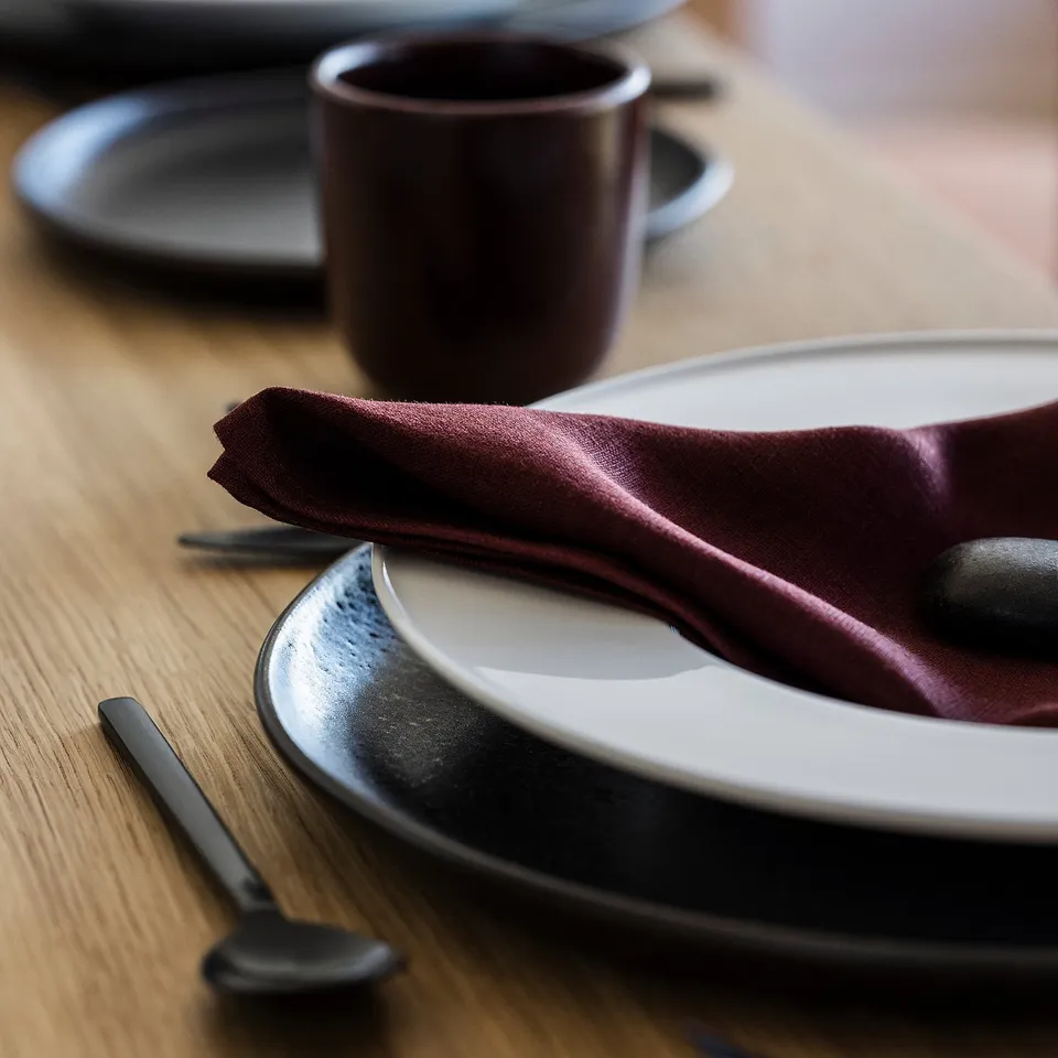 A neatly arranged table setting with a linen napkin, white plate, wooden table.