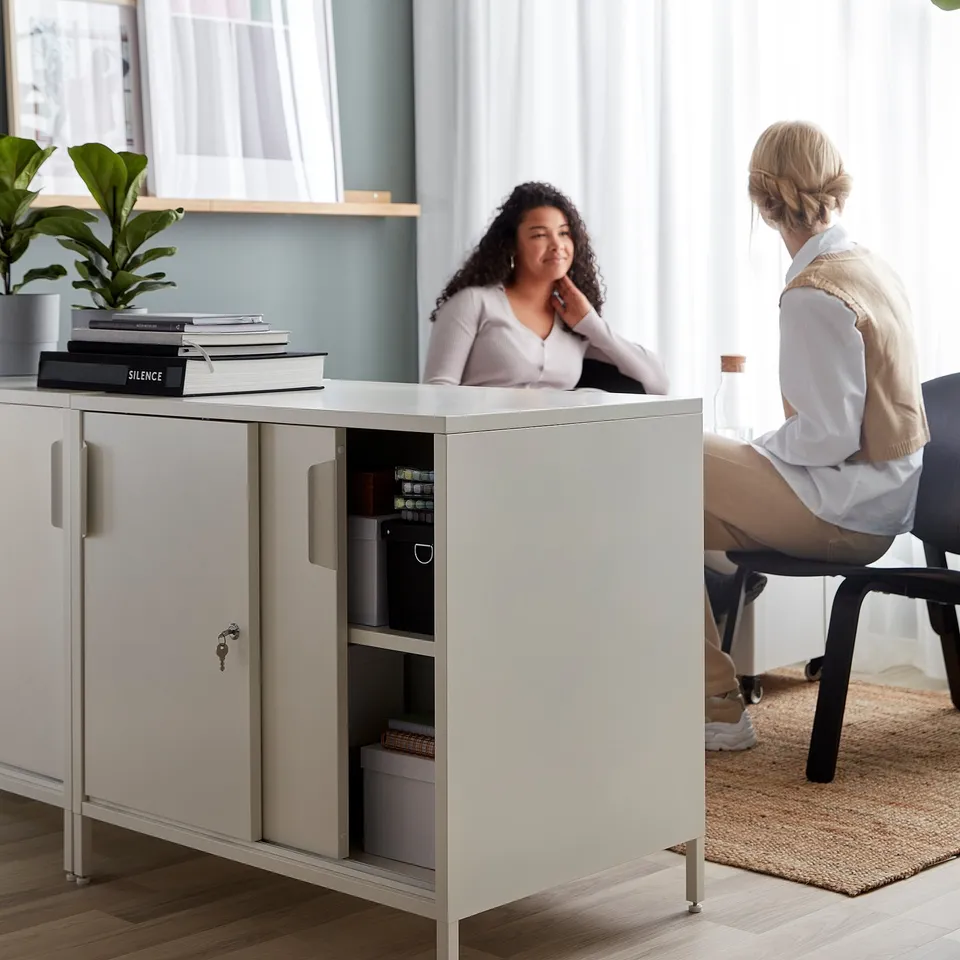 Two people discuss near large white TROTTEN cabinet with safe, in well-lit room.
