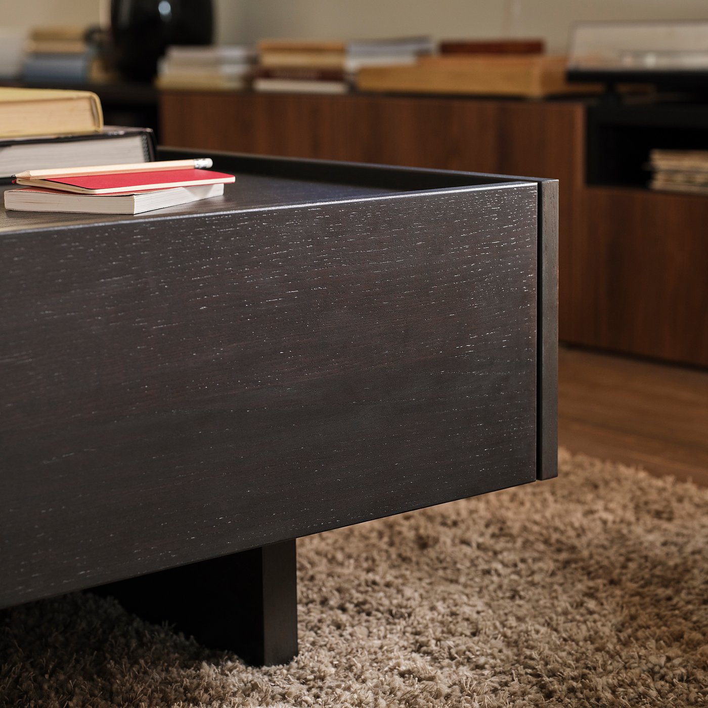 Dark wooden coffee table with visible grain texture, two red books stacked on top, and a soft textured beige rug beneath.
