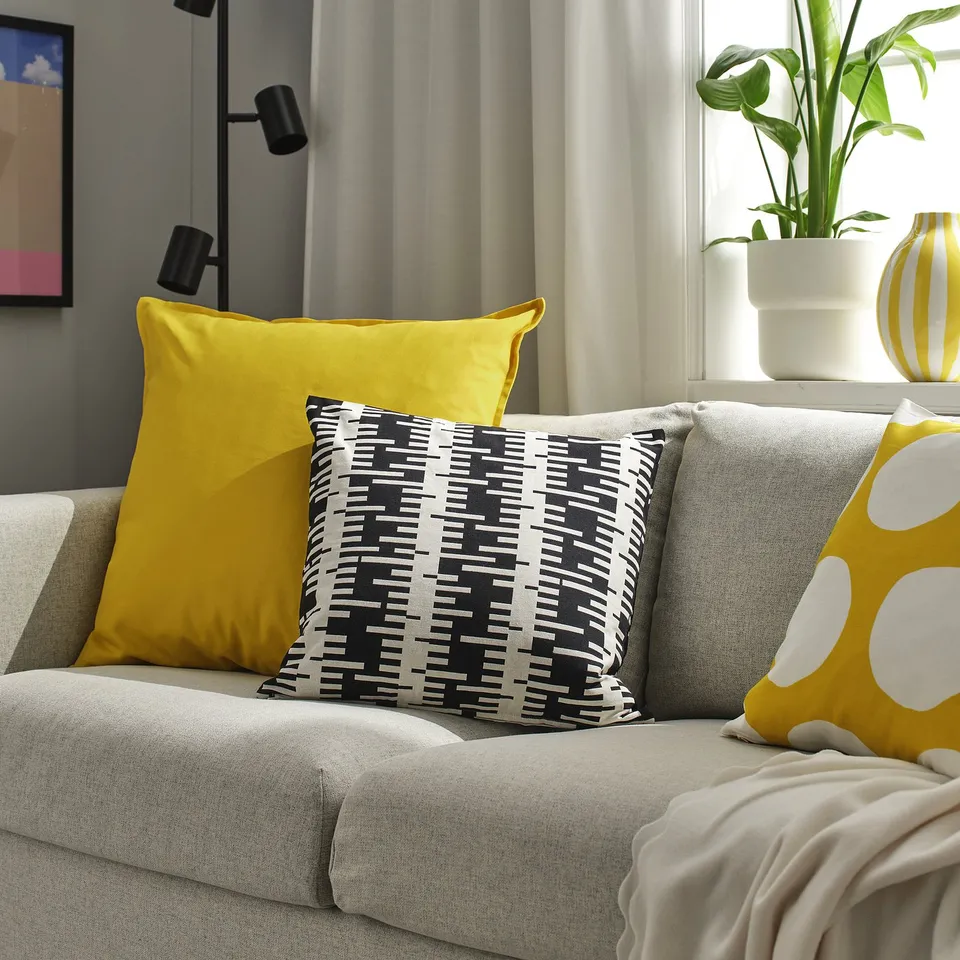 Yellow GURLI cotton cushion on grey couch, with plant and vase in window.