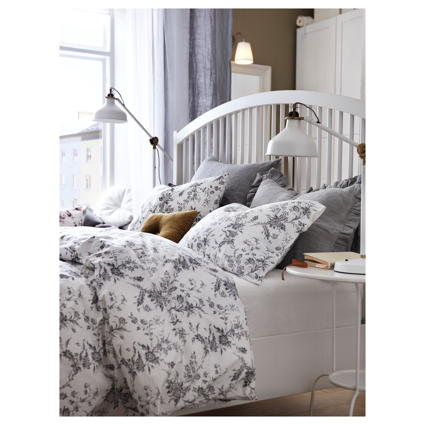 Cosy bedroom with white TYSSEDAL bed, floral linens, grey pillows, bedside lamp, and city view.