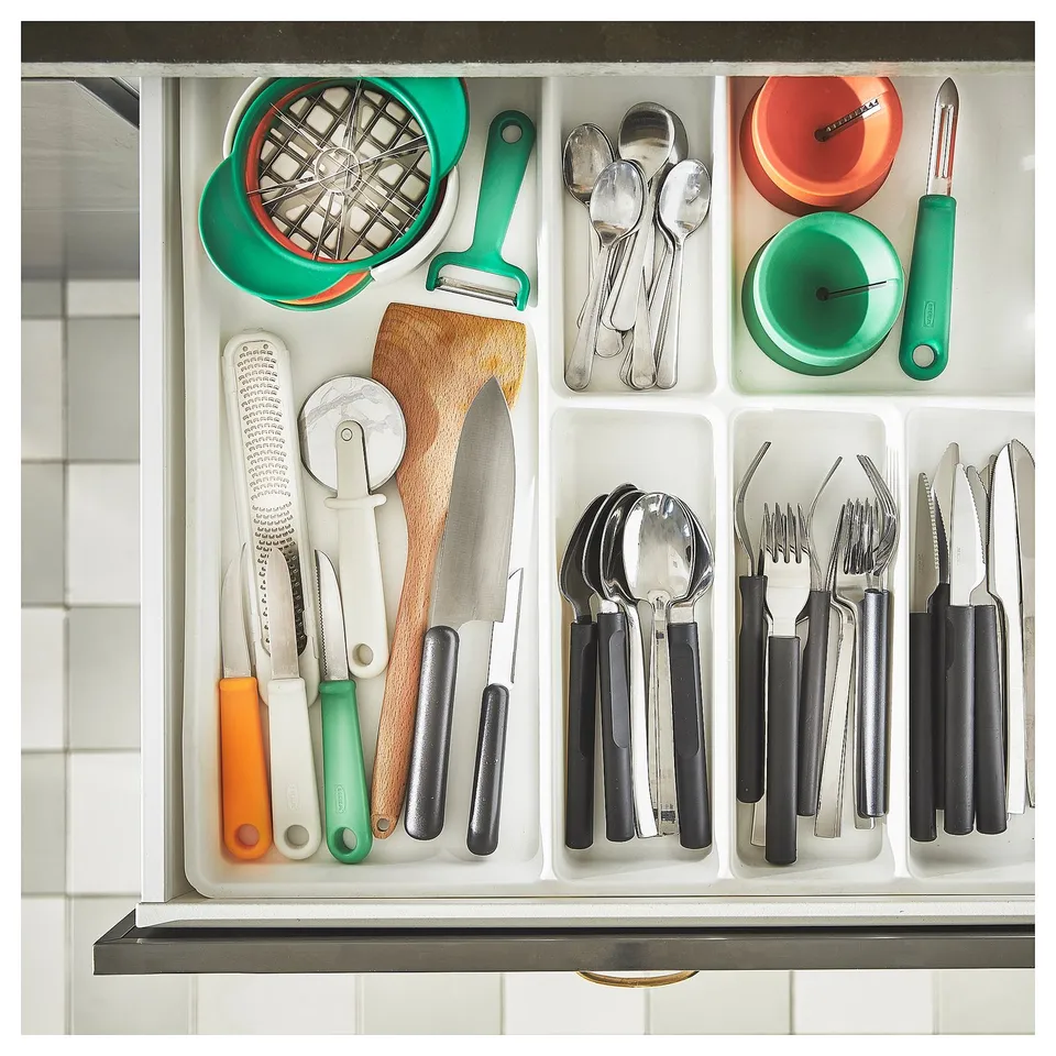 Organised kitchen drawer with colourful utensils and tools, including green and orange fruit cutters, black and silver utensils, and knives.