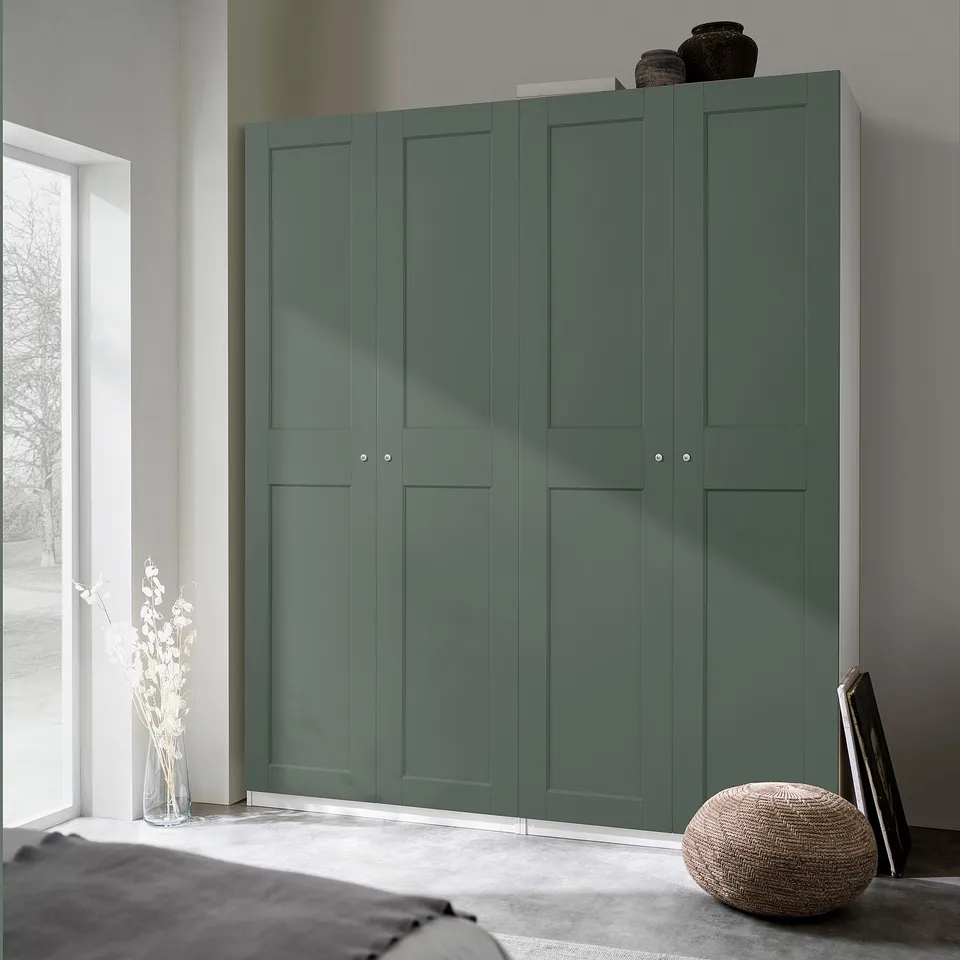 Large teal green wardrobe PAX in bedroom, taller than nearby plants and picture frames, with woven stool and grey bed.