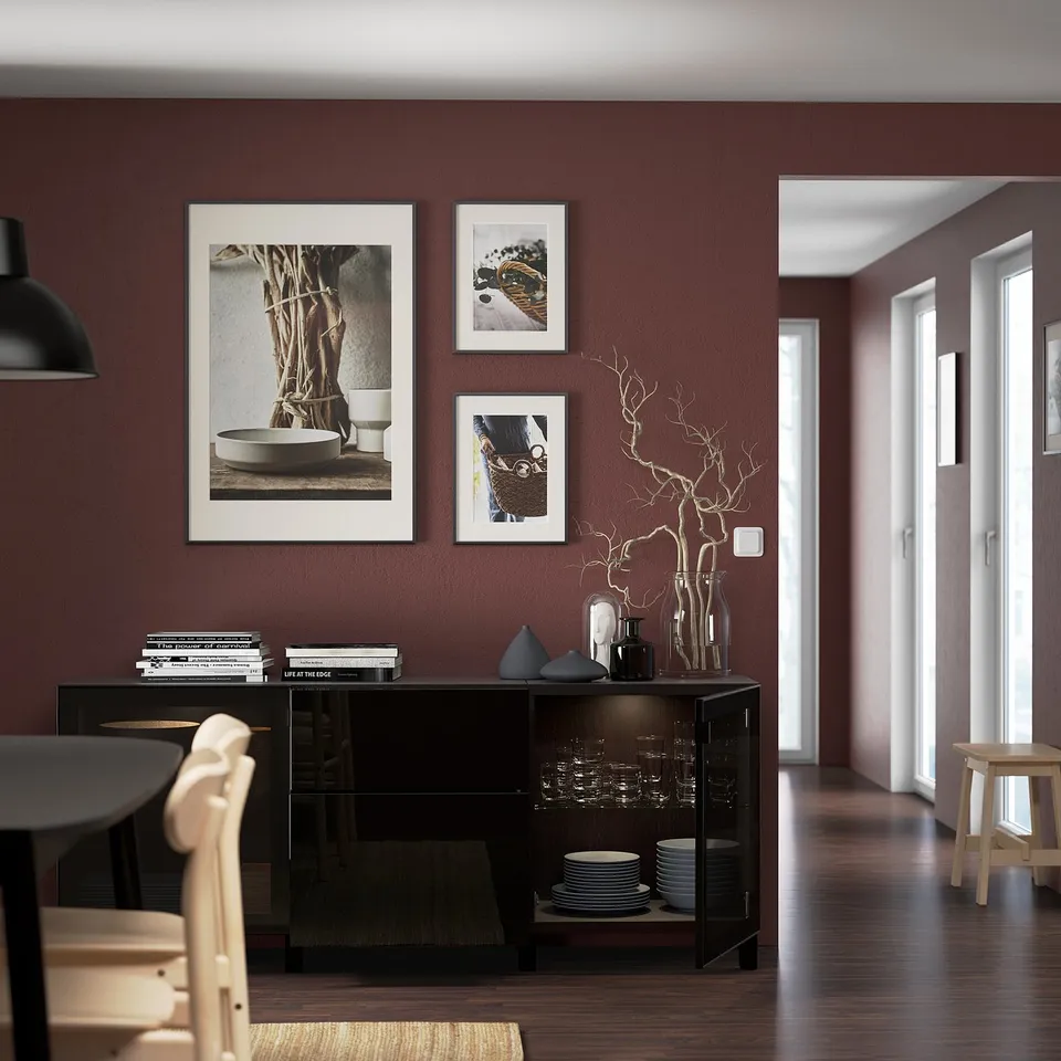 Modern dining area with dark wooden sideboard displaying dishes, vases, and decorative branches. Wall-mounted art and natural light from windows.