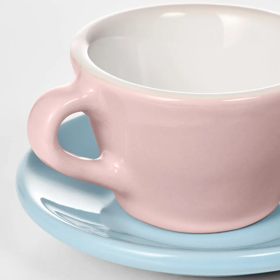 A pastel pink children's mug sits on a light blue saucer, both smooth with even glazing.