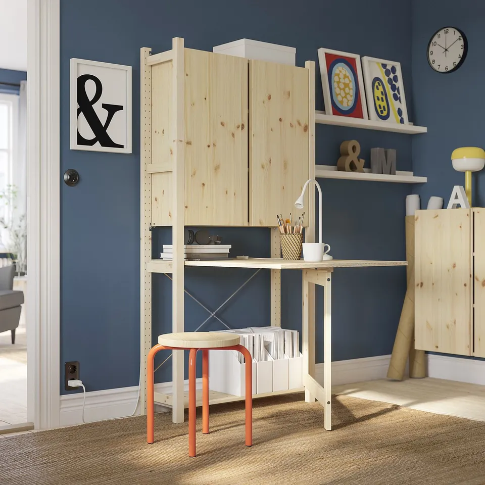 IVAR storage with light wood, industrial shelves, red stool, adjustable desk, dark blue wall.
