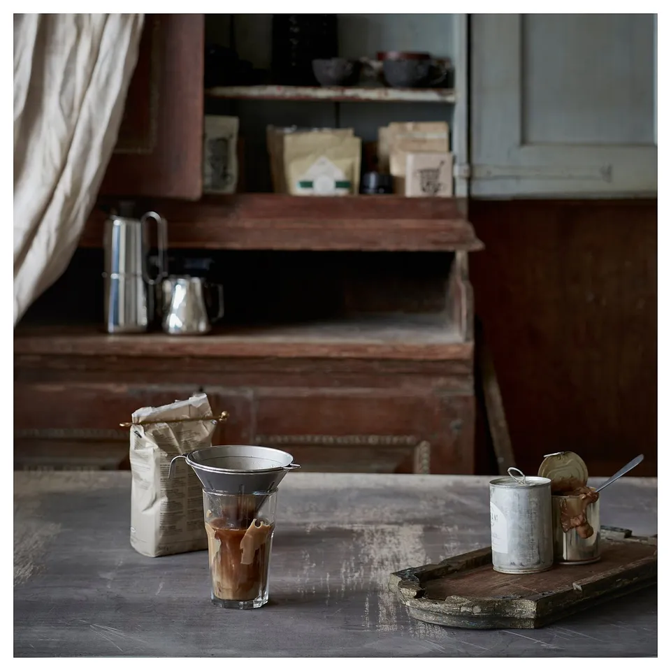 Silver coffee philtre setup on wooden surface next to bags and jars.