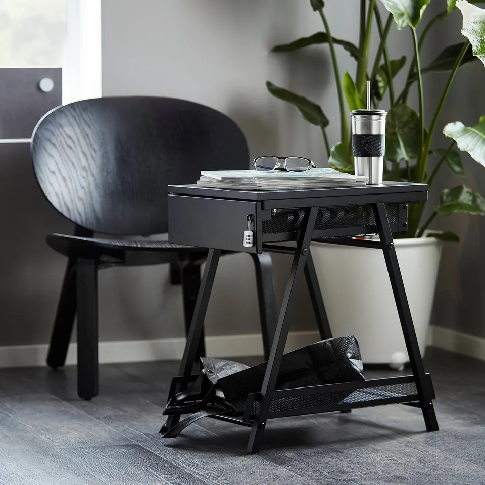 A black TROTTEN storage unit with drawer and shelf, beside a dark wooden chair. Lightweight, durable, space-efficient, ideal for a bicycle helmet.