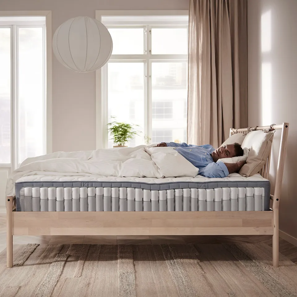 Person sleeps on white VÅGSTRANDA mattress in minimalist bedroom.