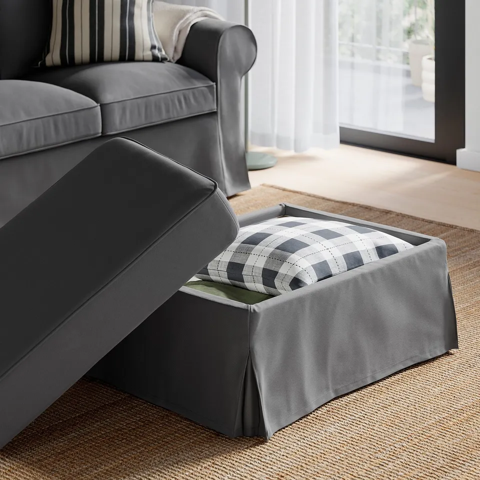 Grey sofa with ottoman, featuring a lift-up seat revealing storage space and a chequered blanket inside.