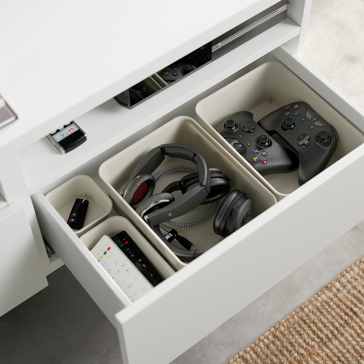 Open white BESTÅ tv drawer revealing organised gaming controllers, headphones, and remotes.
