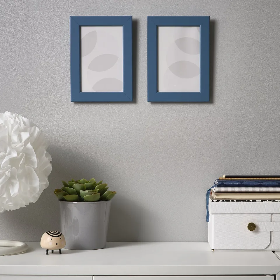 Blue frames on grey wall above desk with plant, decor, figure.