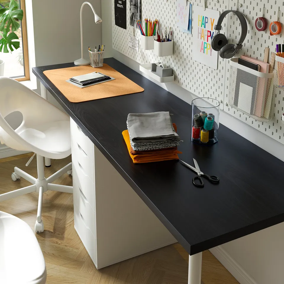 Well-organized home office setup. Black desk with laptop, supplies, and organised pegboard with notes and headphones.