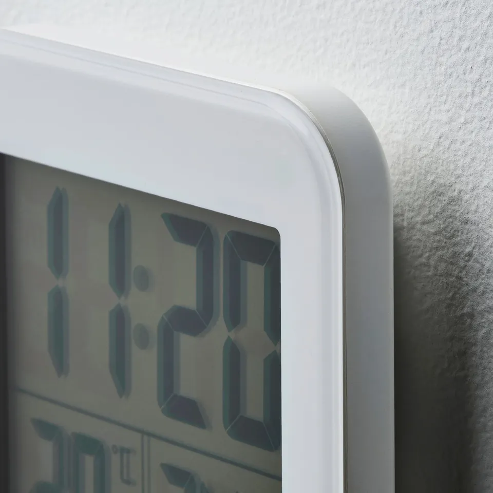 A close-up of a white digital alarm clock, displaying the time as 11:29. The clock is mounted on a wall with a sleek, minimalist design.