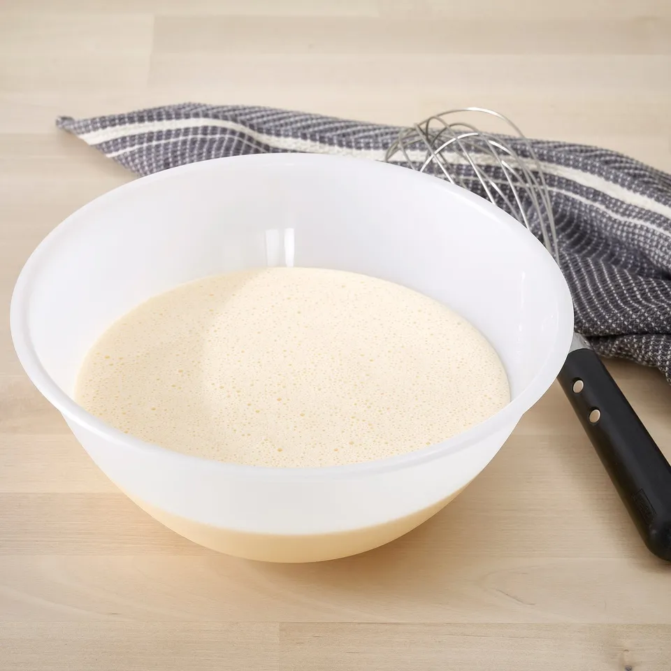 White mixing bowl with batter and whisk on wooden table. Used for baking or cooking.